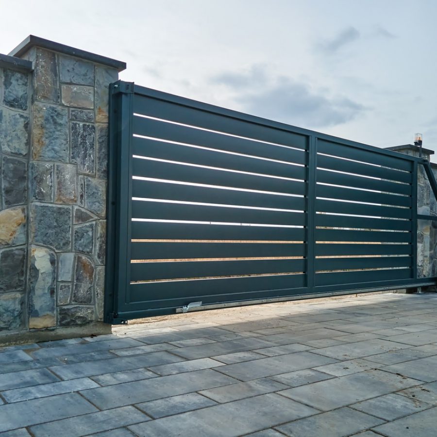 Wide automatic sliding gate with remote control installed in high stone fense wall. Security and protection concept.